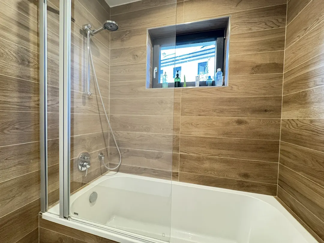 Salle de bains avec baignoire, paroi de douche et petite fenêtre
