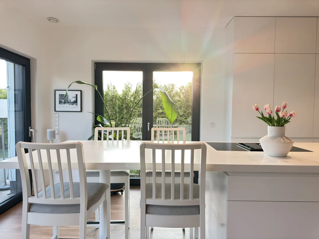 Coin repas avec table et chaises blanches devant la porte-fenêtre