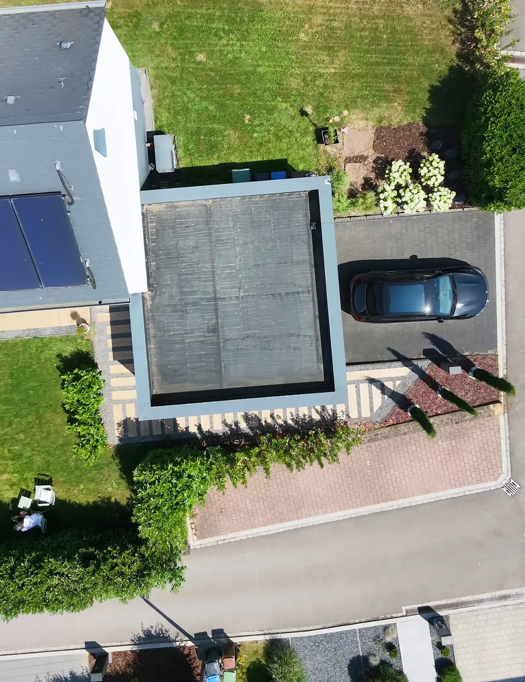 Vue de drone à la verticale : toit du garage, toit de la maison avec panneaux solaires, terrasse et pelouse