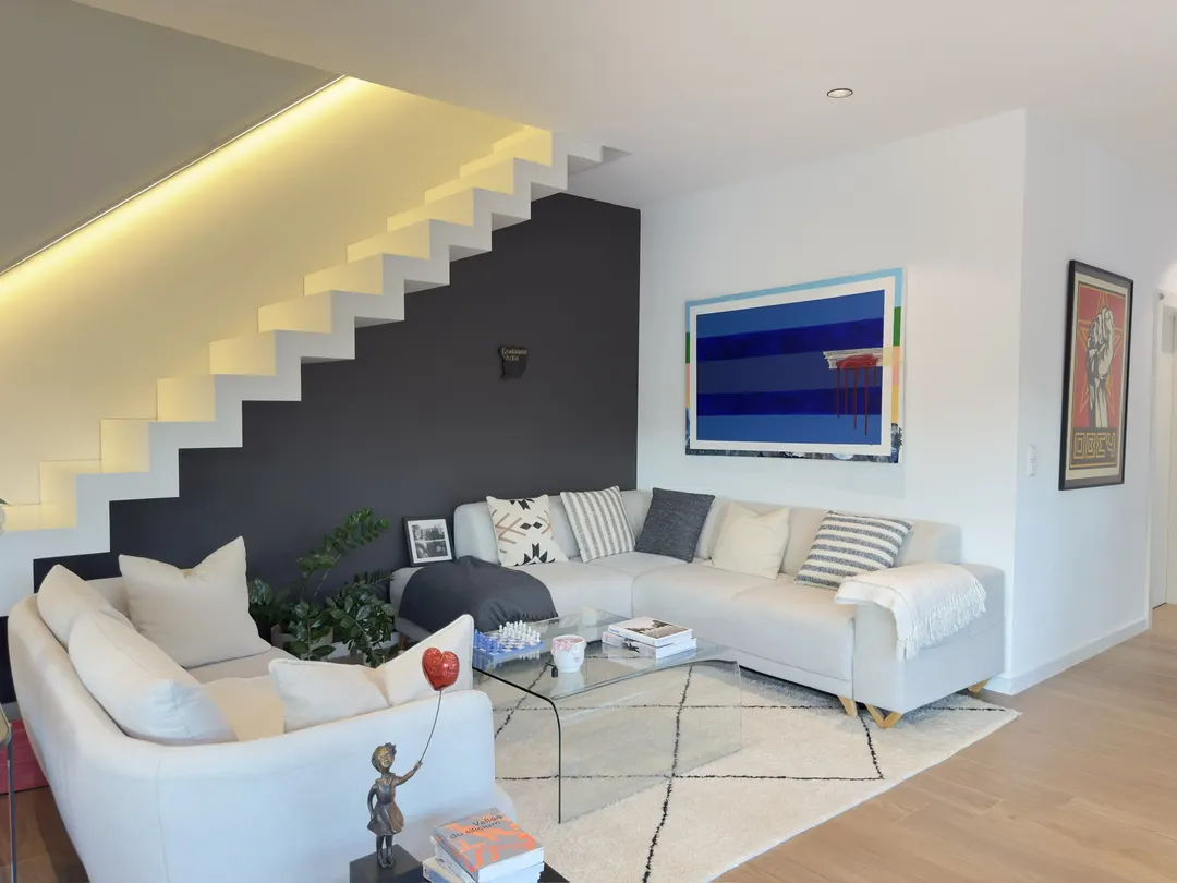 Séjour avec canapés, tapis, escalier blanc au-dessus d'un mur sombre